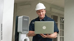 Qualified technician working on home EV charging station installation, making troubleshooting and configuration setup on charging system with laptop for EV at home. Fastidious