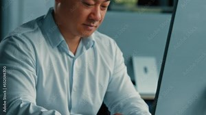 Moving camera male portrait office worker Asian middle-aged man look at monitor work online on computer develop program search business information use internet texting e-mail virtual communication