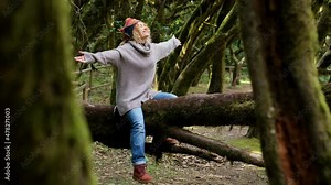 Happy adult female sitting on a trunk tree in forest woods enjoy wild nature park outdoors, alone opening arms - overjoyed female people in freedom and joyful - people and inner balance concept life