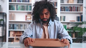 Unhappy young Indian man frustrated by received parcel unpacking box and gets upset about wrong order online shopping or damaged package, bad delivery service. Unsuccessful purchase concept.