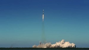 Rocket lifts off from launch pad and rises into a clear blue sky. Wide shot. Slow-motion with sound.