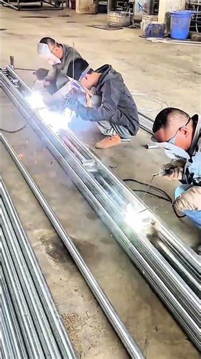 Three welders join parallel pipes in busy workshop