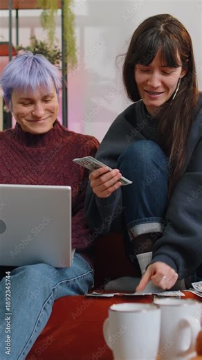 Planning budget. Rich happy two young lesbian women family couple counting money cash use laptop computer calculate domestic bills at home living room. Girls friends satisfied of income earnings
