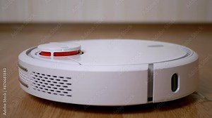 A Modern Automatic Robot Vacuum Cleaner Sweeps the Floor in Room. A round white vacuum cleaner with small brushes, touch motion sensor. Autonomous room cleaning on the remote control. Smart House.