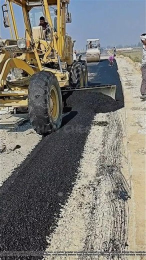 A motor grader is leveling asphalt concrete on the edge of the road.