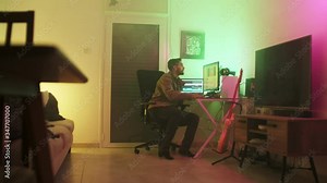 video editor freelancer sitting his black chair, hands typing, editing videos at his desk in a foggy room, wearing a beige brown jacket, clicking his mouse. dolly-in shot.