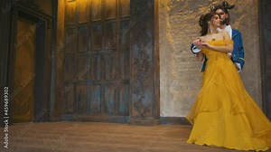 Fairytale couple dancing in ancient medieval castle. Fantasy woman, vintage yellow long evening dress. Enchanted prince man in blue antique jacket, black trousers. Ram horns on brunette hair