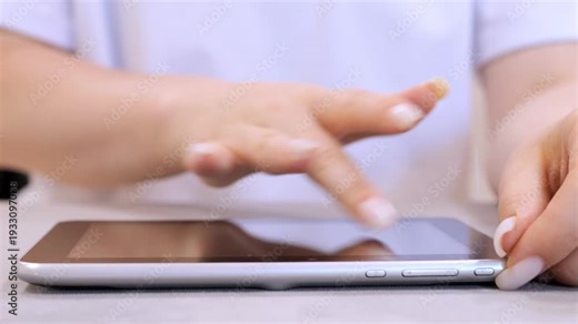 Woman is using a tablet. She is touching the screen with her fingers. The tablet is silver and rectangular