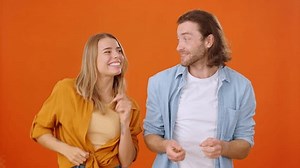 Energetic man and woman dancing in place modern dance performing different movements on orange background of premise. Positive emotions and active lifestyle