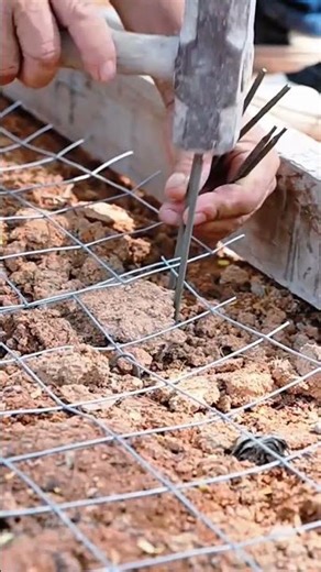 Worker securing steel wire mesh foundation using hammer and pliers