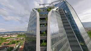 Fpv dive shot of a tower in city, mountains and trees on the background during soft light afternoon