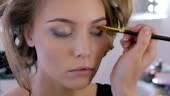 Professional make-up artist applies eye shadow to eyelid of model....