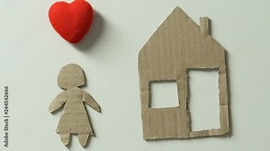 Hand adding house figure and toy heart to paper child, dreaming about home