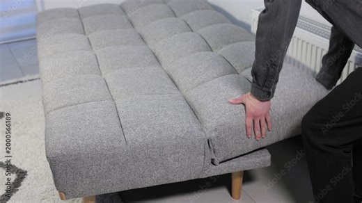 Person folding a grey sofa bed from a sleeping position back into a comfortable sitting sofa in a living room.