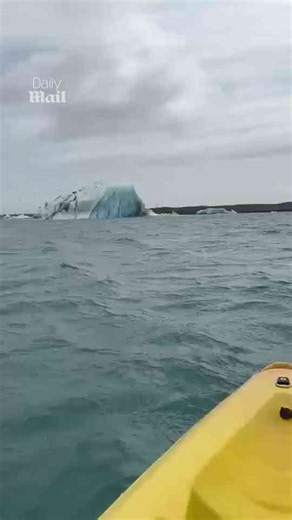Kayakers paddle alongside towering iceberg