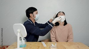 4K, Asian couple uses a rapid antigen test kit to self-test the COVID-19 at home. A long cotton swab is inserted into the nose and internal nasal fluid sample for COVID-19 testing.