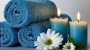 Blue towels are rolled up and arranged with lit blue candles and white daisies