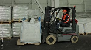 Warehouse organization, Stock arrangement, Operator skills. Warehouse employee is working alongside forklift loader to navigate pallets.