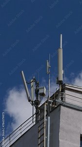 Mobile phone communication tower on building roof on blue sky with clouds background. Technology of telecommunication GSM tower (5G,4G,3G concept). Time lapse footage