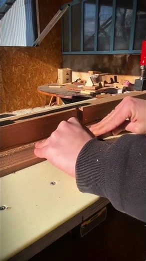 Creating precise wood joints using a router table and careful hand movements in a sunny workshop