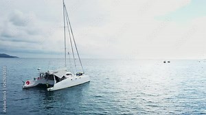 Top view of the boat. Aerial View of a Anchored Catamaran Yacht Standing and people can Sunbathing on it's Deck. Runabout or cruiser stands in azure Sea Waters With Coral Reef Visible. Weekender from