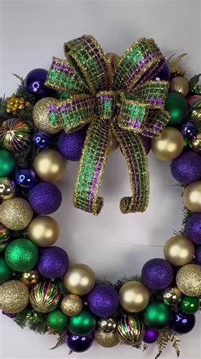 Celebrate Mardi Gras in grand style with this luxurious Mardi Gras ornament wreath, handcrafted on a lush evergreen wreath and bursting with festive purple, green, and gold! Designed to make a bold statement, this wreath is full, vibrant, and eye-catching—perfect for welcoming guests with true carnival flair. It has a small strand with 20 mini bulbs of battery operated lights. It also has a large beautiful full bow! This wreath is loaded with shimmering Mardi Gras ornaments, rich textures, and l