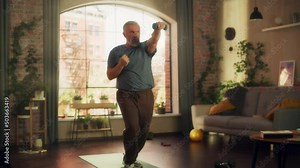 Strong Athletic Fit Senior Man Doing Cardio Core Strengthening Exercises with Dumbbells During Morning Workout at Home in Sunny Apartment. Fitness and Recreation Concept. Zoom Out Shot.