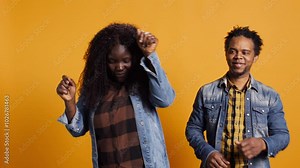 Lovely cheerful husband and wife dancing around in the studio and having fun together, acting silly with groovy funny dance moves against yellow background. Funky married people. Camera B.