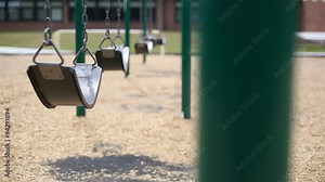 Swing School Background Selective Focus. 2 shots: empty swings swaying in the breeze at a playground with a school in the background. a single swing swaying faster closest to the camera