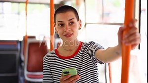Beautiful, young short-haired woman riding in a city bus and using smartphone