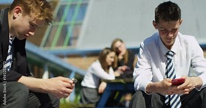 4k,Two male students in school uniforms looking at their smartphone during a b