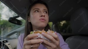 Woman eating burger in the front seat of the car during the morning journey. Car, vehicle, automobile.