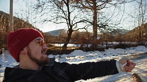 Handsome young bearded man riding on sledge or ice-boat tied to a car traveling through nice winter landscape in the mountains.