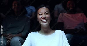 A Chinese woman laughing uncontrollably as she watches a comedy at the movie theatre.