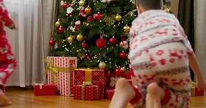Children opening Christmas presents by festive tree
