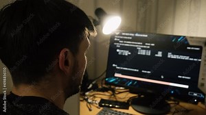 Hacker, programmer, guy smokes electronic cigar, front computer screen. It waiting for download and installation program completed computer. He exhales smoke light table lamp. Handheld shooting