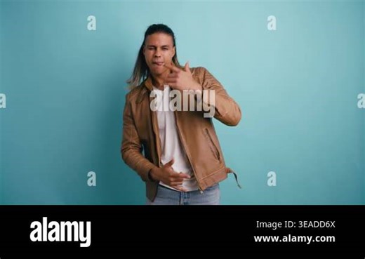 Young man with long hair wearing a brown leather jacket singing and dancing energetically, looking at the camera against a turquoise background Stock Video Footage - Alamy