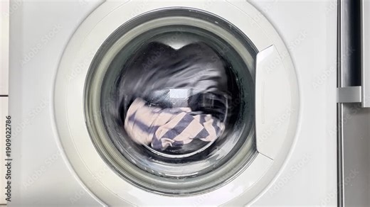 A white washing machine with a load of clothes inside. The machine is spinning