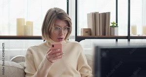 Woman text messaging on mobile phone while watching tv at home