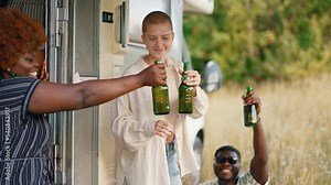 Young adult group of friends hanging out outside camper van talking and cheering with beer bottles. Diverse friend group camping. Horizontal outdoor video. High quality 4k footage