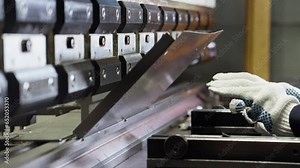 Bending machine operator bends sheet metal product. Employee works at metal factory. Bending sheet metal on hydraulic machine. Close-up in 4K, UHD