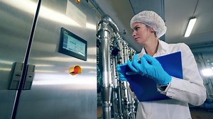 Plant worker checks a machine, typing on display. Female worker controls the quality of production equipment.