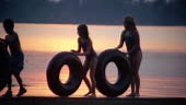 Slow motion three children rolling inner tubes down pier at sunset...