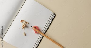 Overhead view of open notebook with pencil and pencil sharpener on beige background, in slow motion