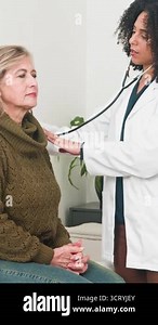 A professional female doctor is performing a thorough medical examination on a senior female patient in a bright clinic room. She uses a stethoscope to check the patients heart and lungs, promoting health and wellness.