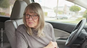 Lost senior Caucasian woman driver looking for building address and checking map app on her smartphone while in parked car. Older woman text messaging on smartphone before driving. Slow motion 4k
