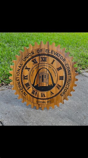 This custom-designed 24" teak wood elevator clock is a stunning tribute to craftsmanship, tradition, and pride in the trade. Expertly carved from rich, durable teak, the piece showcases the emblem of the International Union of Elevator Constructors with remarkable detail and precision. Its gear-shaped design and engraved Roman numerals pay homage to the mechanical artistry of the elevator industry, while the natural wood grain adds warmth and timeless elegance. Perfect as a display piece for uni