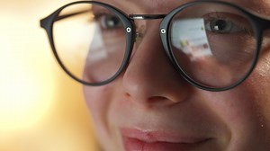 Woman in glasses looking on the monitor and surfing Internet at night. The monitor screen is reflected in the glasses. Work at night. Home Office. Remote work