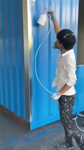 spraying blue paint on a shipping container wall surface