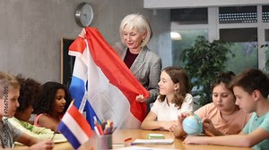 Friendly high school teacher, conducting a lesson in the classroom, tells pupils the history of the Netherlands and holds the national flag of the country in her hands. High quality 4k footage